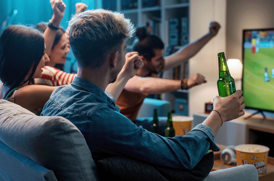 Freunde sitzen auf Sofa und sehen Sport im Livestream